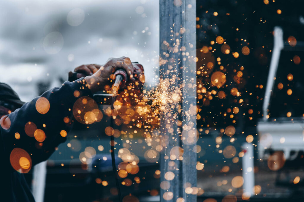 A person uses a power tool to grind metal, creating bright orange sparks that scatter in various directions.