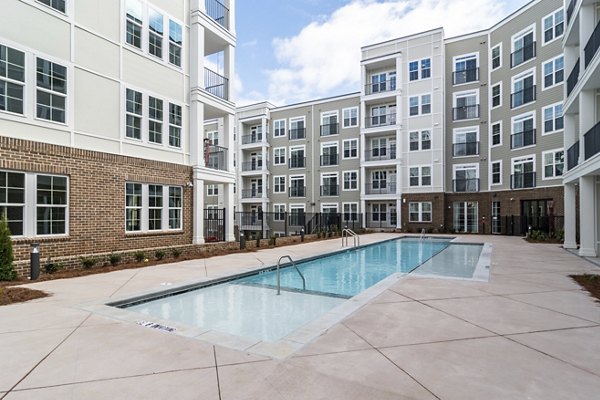 Rectangular outdoor swimming pool in the courtyard of a modern apartment complex with multiple floors and balconies.