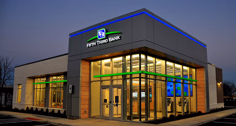 Modern Fifth Third Bank branch with large windows and illuminated signage, pictured at dusk with interior lights visible.