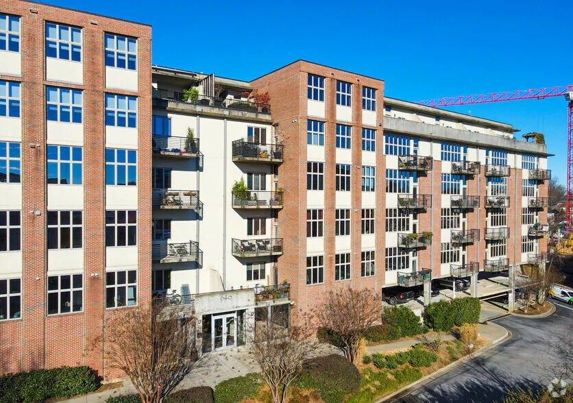 A multi-story apartment building with brick and light-colored exterior walls, balconies, and large windows under a clear blue sky.