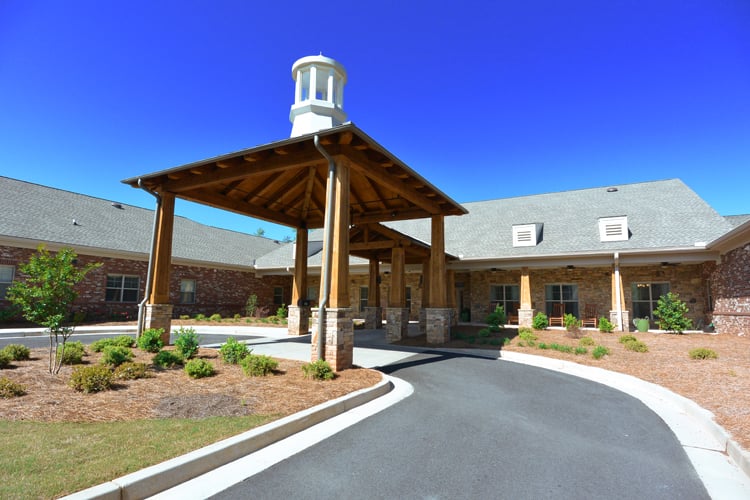 A single-story brick building with a covered entrance and landscaped driveway under a clear blue sky.