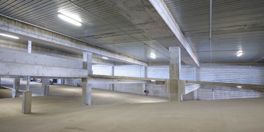 Interior view of an empty multi-level concrete parking garage with pillars and fluorescent ceiling lights.