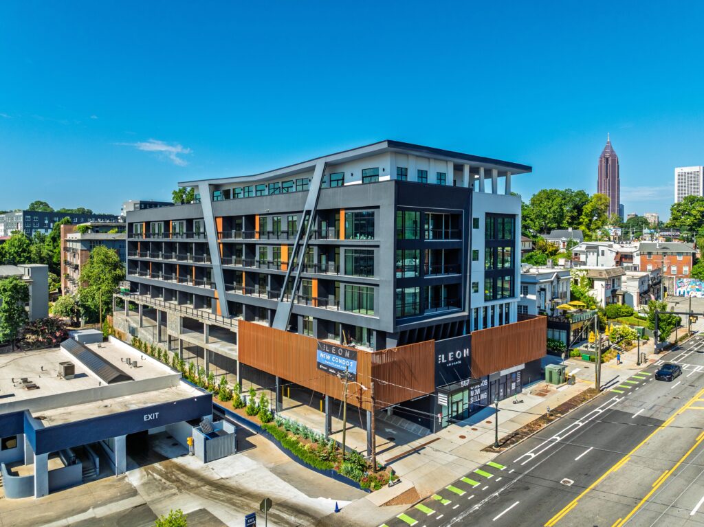 A modern multi-story apartment building with balconies, large windows, and a rooftop terrace, located on a city street with bike lanes and an exit ramp visible.