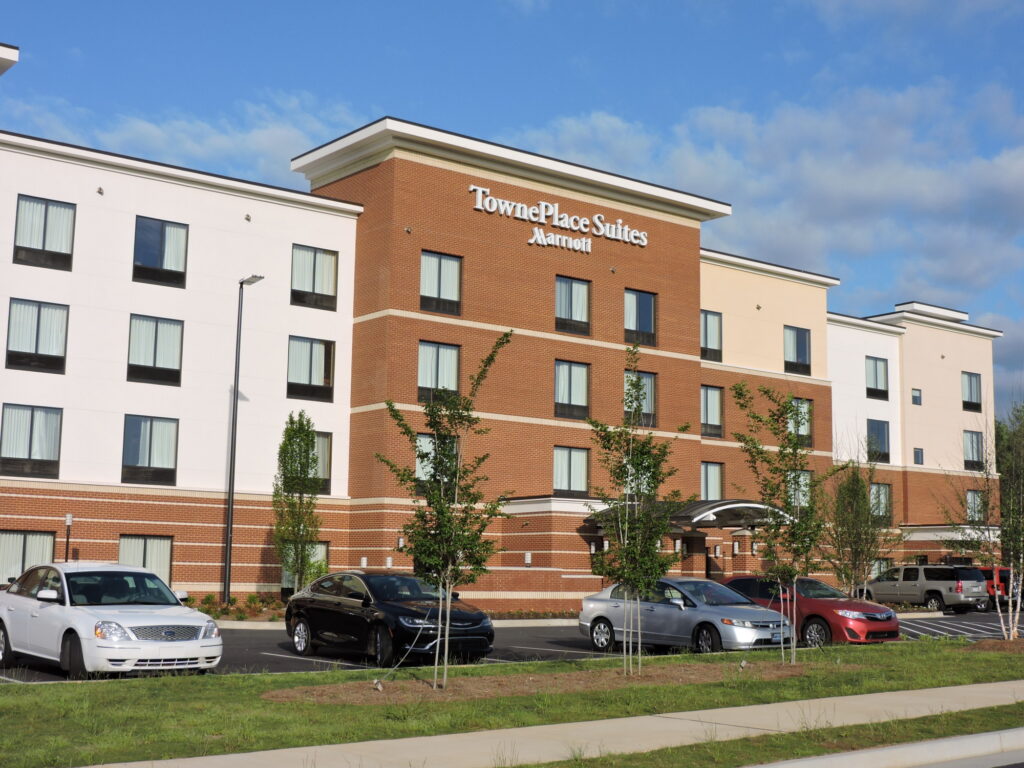 TownePlace Suites by Marriott hotel building with four stories, large windows, and several parked cars in front under a partly cloudy sky.