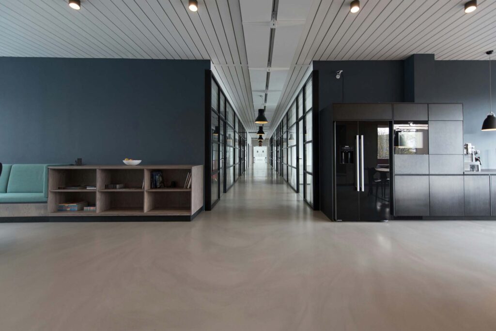 Modern office hallway representing the markets Summit Electrical Group supports, with glass-walled rooms, built-in seating, shelves, and a kitchenette with appliances.